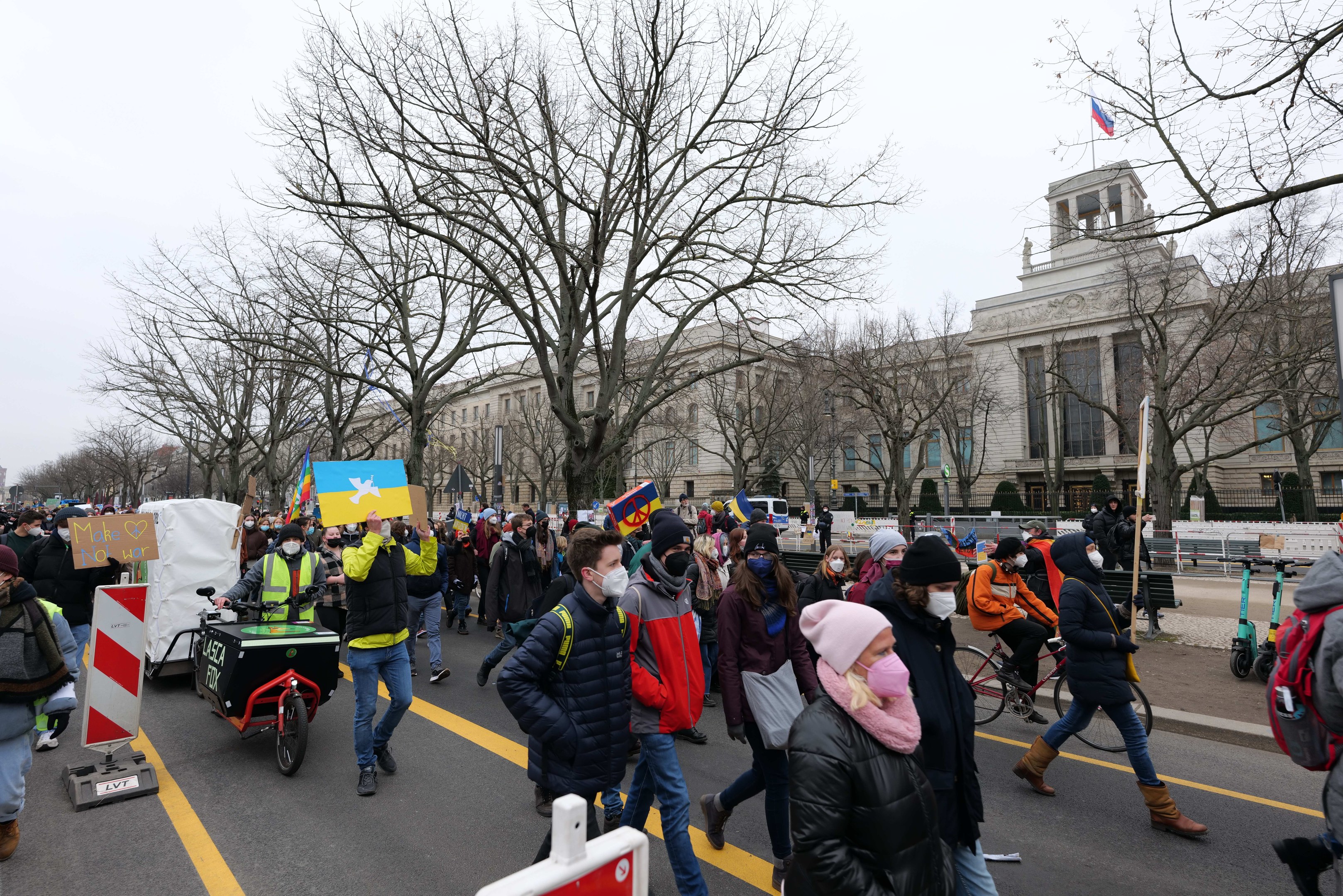 Eine große Gruppe von Menschen nimmt an einer Protestdemo in Washington, D.C. am 21. Januar 2020 teil und marschiert eine Straße entlang, wobei einige Schilder und Banner halten und andere Fahrräder fahren, mit Schildern, Bäumen und einem klaren blauen Himmel im Hintergrund.