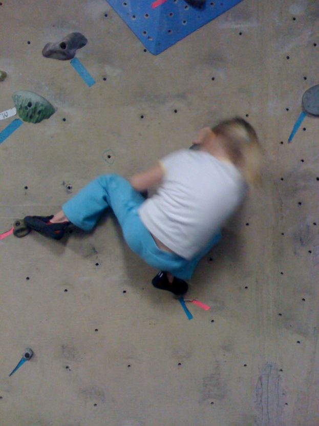Ein Kind klettert an einer Boulderwand hoch.