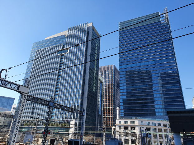 Eine Stadtstraße mit hohen Gebäuden, Strommasten, Drähten, Straßenlaternen, Verkehrsampeln, Namensschildern, Bäumen und einem klaren blauen Himmel.