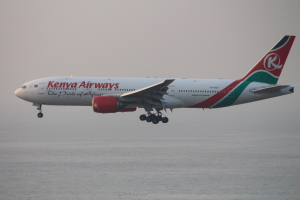 Airbus A330-300 der Kenya Airways im Flug mit weißer, roter und grüner Lackierung vor einem blauen Himmel und glitzerndem Wasser darunter.