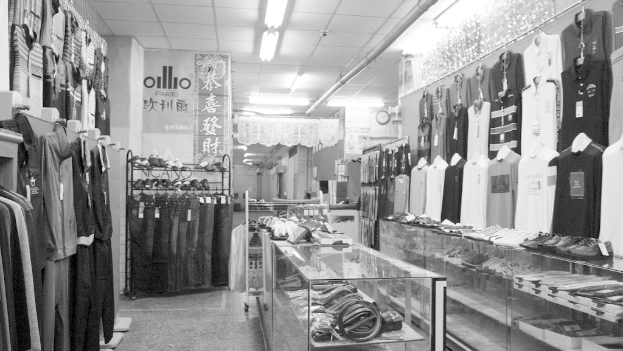 Eine Anzeige von Kleidung, Gürteln und Schuhen mit einer Uhr an der Wand, hängendem Stoff, Lampen und einem Banner mit Text auf der linken Seite.