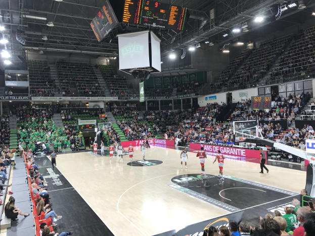 Basketballspiel in einer großen Arena mit Zuschauern, mit einem Scoreboard, das "Asvel vs Galatasaray" während des Spiels anzeigt.