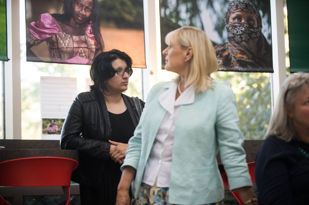 Drei Frauen, eine sitzend auf einem Stuhl, mit zwei Stühlen, einer Glastür, einem Vorhang und einem Baum im Hintergrund.