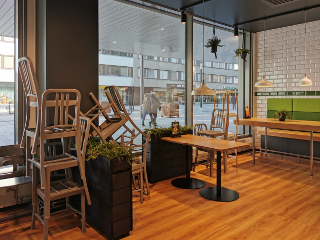 Ein Restaurantinnenraum mit Holztischen und -stühlen in der Nähe eines großen Fensters, das auf eine Berliner Straße mit Fußgängern, Gebäuden und Straßenelementen blickt.