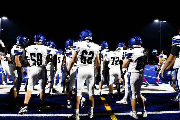 Gruppe von Fussballspielern in Helmen und Stiefeln auf einem Feld unter Flutlicht.