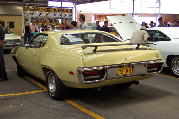 Ein Oldtimer fährt auf einer Straße mit Menschen, Geschäften und Gebäuden im Hintergrund.