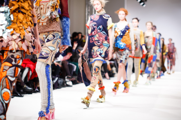 Eine Gruppe Von Frauen Geht Den Laufsteg In London Fashion Week, Mit Einer Zuschauerschaft Im Hintergrund Unter Helllem Licht.