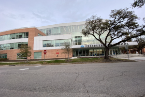 Großes, zweistöckiges Backsteingebäude mit der Aufschrift "Presbyte Middle School" und vielen rechteckigen Fenstern, umgeben von Bäumen, Gras, Schildern, Strommasten und einer asphaltierten Straße unter einem bewölkten Himmel.