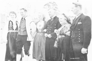 Eine Gruppe von Menschen aus den 1930er Jahren, die zusammenstehen, lächeln und im Hintergrund Bäume zu sehen sind, mit dem Text "Bayerische Familie in den 1930er Jahren" unten.