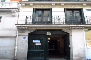 Ein Gebäude mit einer grünen Tür, Fenstern, Geländern, Lampen, Texttafeln, einem Rohr und anderen Gegenständen, mit einer Straße unten.