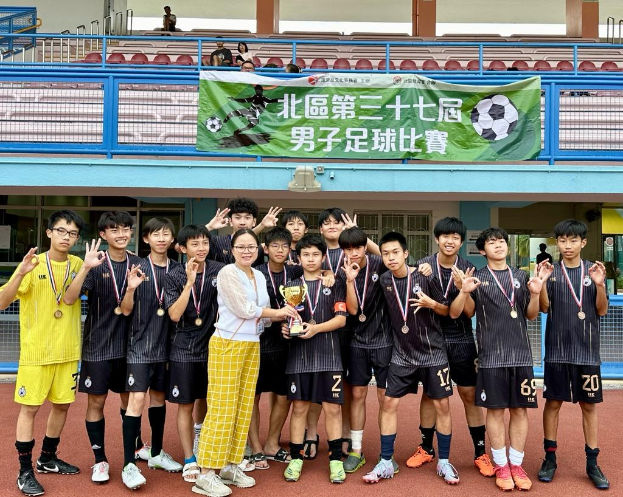 Eine Gruppe junger Männer in Fußballtrikots steht auf einem Feld und hält einen Pokal, während sie Medaillen tragen und ein Banner für die "Yokohama U-16 Jungenfußballmannschaft" im Hintergrund zu sehen ist.