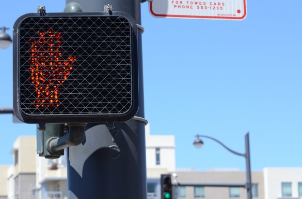Eine Stadtstraße mit Verkehrspfosten, Ampeln, Straßenlaternen, Gebäuden und einem klaren Himmel.