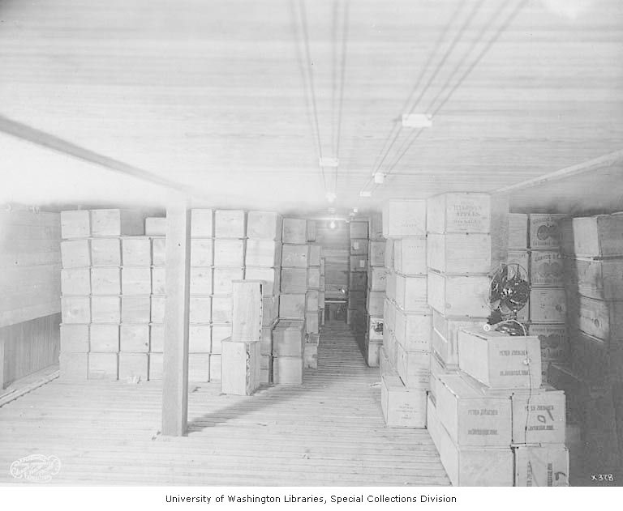 Ein Schwarz-Weiß-Foto eines Raums voller Kartons auf dem Boden und an den Wänden, beleuchtet von Deckenlampen, mit dem Text "Bibliothek des Kongresses, Washington, D.C." unten.