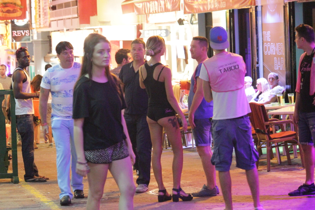 Eine Gruppe von Menschen, die an Tischen und Stühlen in einem Raum mit Gläsern, Geschäften, Schildern, Tafeln und Lampen steht und sitzt.