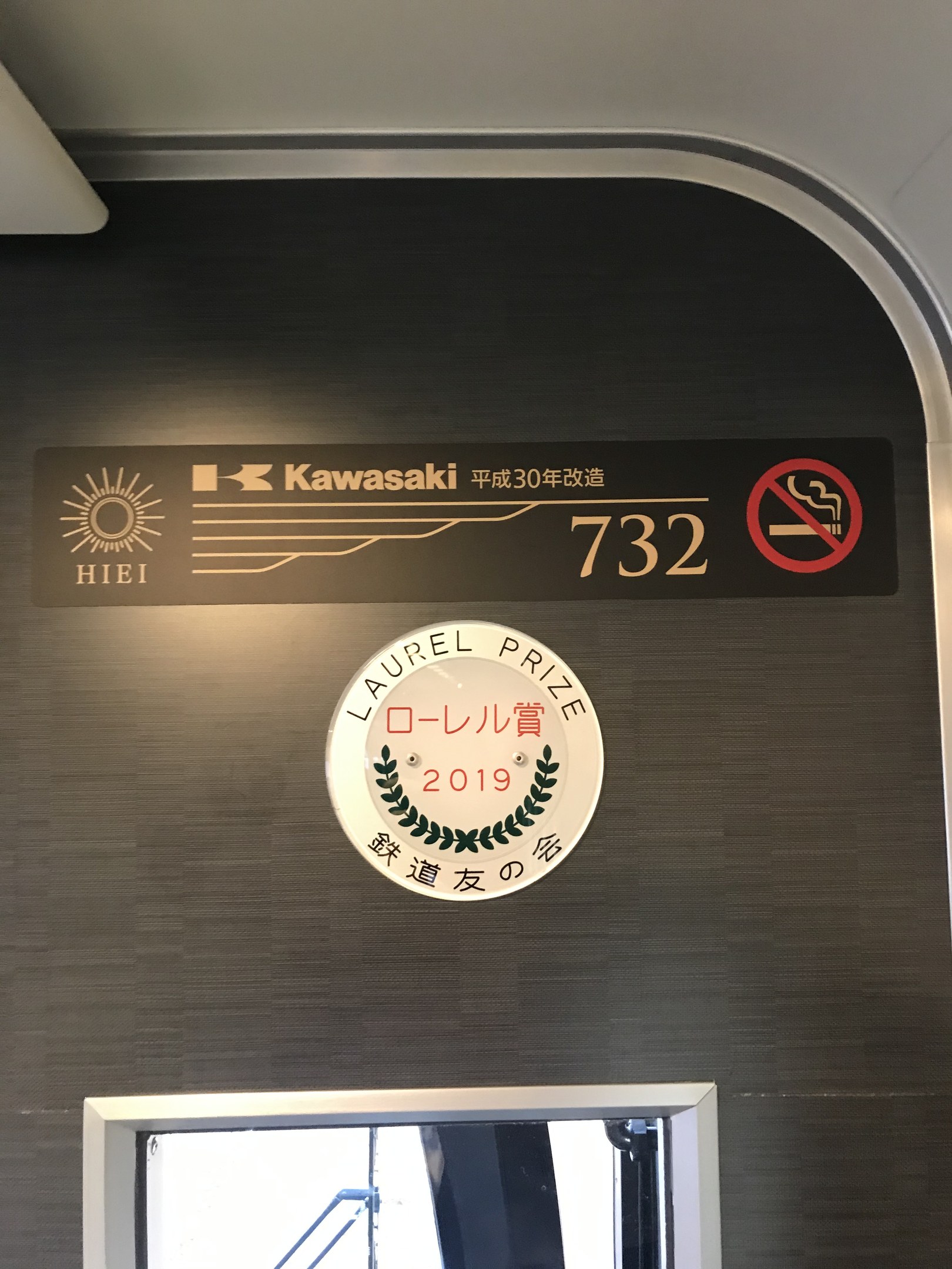 Wand mit einem Schild, auf dem "Kawasaki 732" steht und ein Glasfenster rechts daneben.