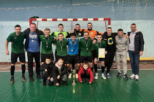 Eine Gruppe von Männern in Medaillen, einer hält einen Pokal, steht auf einem Futsal-Platz mit einem Tor und einer Wand im Hintergrund und feiert ihren Futsal-Weltmeisterschaftssieg.