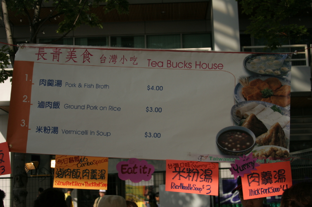 Eine Fahne mit Papiernotizen vor Gebäuden, Fenstern und Bäumen, mit einem Zaun und Menschen unten.