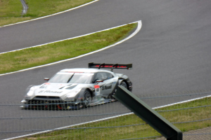 Audi R8 LMS GT3 auf der Nürburgring 24 Stunden Rennstrecke, umgeben von einem Metallzaun und saftigem Grün, in der Mitte positioniert mit der Strecke, die sich vor ihr erstreckt.