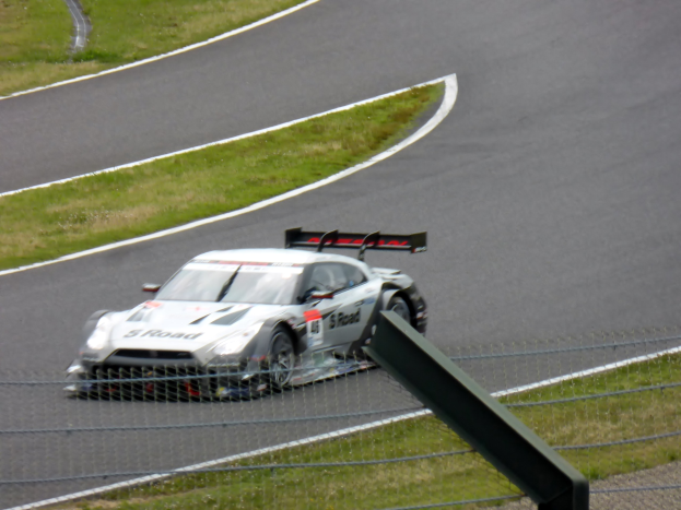 Audi R8 LMS GT3 auf der Nürburgring 24 Stunden Rennstrecke, umgeben von einem Metallzaun und saftigem Grün, in der Mitte positioniert mit der Strecke, die sich vor ihr erstreckt.