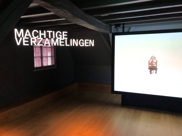 Installationsansicht der Ausstellung "Machtige Verzamelingen" im Museum of Modern Art in Berlin, mit einem großen Bildschirm auf der rechten Seite und einem Fenster auf der linken Seite.