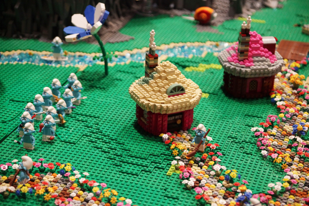 Ein LEGO-Modell einer Kleinstadt mit bunten Blumen, Häusern, Spielzeugen, Pflanzen und anderen Gegenständen vor einem leicht unscharfen Hintergrund.