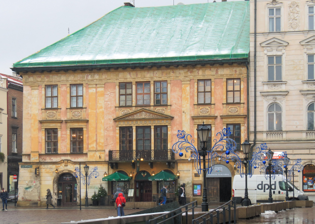 Großes grünoberes Gebäude in städtischer Umgebung mit Straßeninfrastruktur, Fahrzeugen, Fußgängern, Bäumen und klarem Himmel.