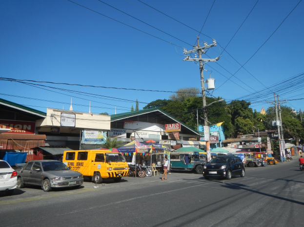 Vollständige Straße mit Autos, Motorrädern, Fußgängern, Zelten, Gebäuden, Strommasten, Bäumen und einem klaren blauen Himmel.