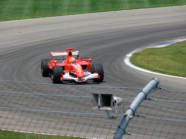 Ein Fahrzeug fährt auf einer von Gras umgebenen Straße mit einem Maschendrahtzaun.