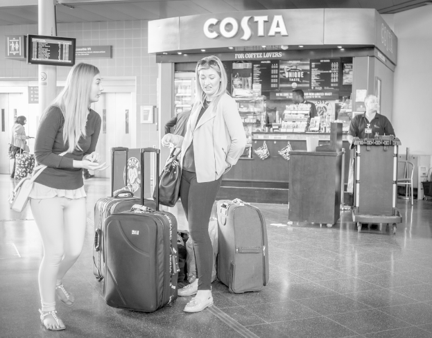 Zwei Frauen vor Gepäckstücken mit einem Kaffee-Shop im Hintergrund, wahrscheinlich an einem Flughafen.