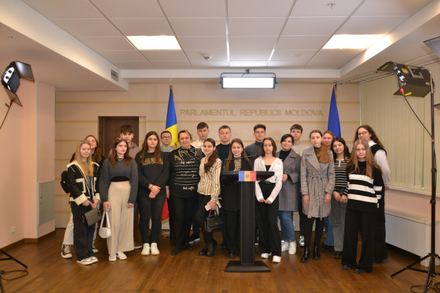 Gruppe von Menschen vor einem Rednerpult mit Mikrofon auf dem "Moldova Youth Congress 2018"-Event, umgeben von Fahnen, einer Wand mit Text, einer Tür, Deckenleuchten und Scheinwerferstativen.