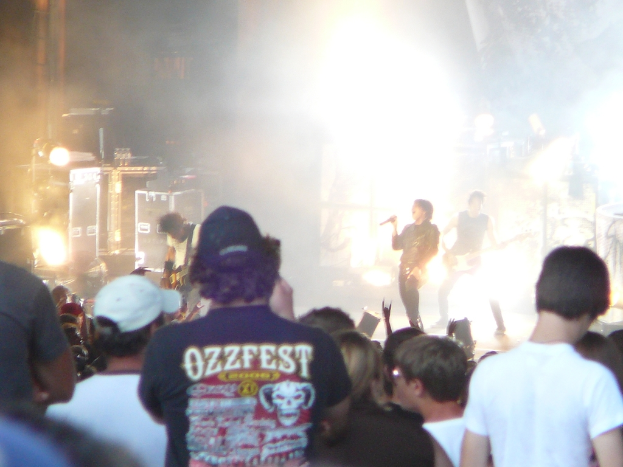 Eine Gruppe von Menschen in verschiedenen Kleidungsstücken, einige mit Mützen, in der Nähe von Musikinstrumenten wie einer Gitarre und einem Mikrofon sowie Bühnenscheinwerfern.