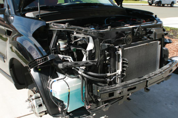 Ein Auto mit offenem Motor steht geparkt da, mit einem anderen Auto oben rechts im Bild.