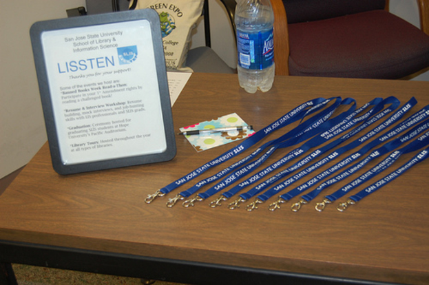 Ein Tisch mit ID-Kartenhaltern, ein Foto Rahmen, eine Karte, ein Stift, eine Wasserflasche und ein Stuhl mit einer Tasche darauf.