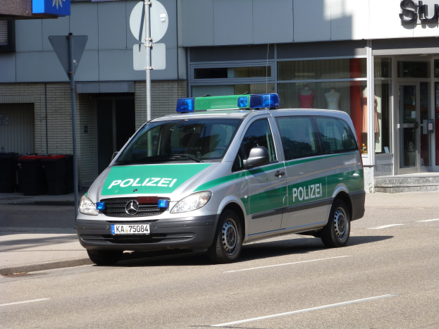 Polizeifahrzeug auf der Straße vor einem Gebäude mit Glastüren und Schaufensterpuppen geparkt.