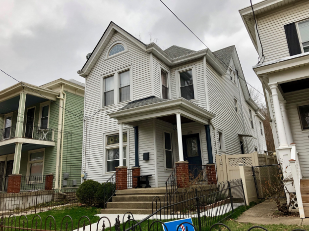 Reihe von Häusern mit Fenstern, Türen, Säulen, Geländern, Treppen und Dächern, umgeben von einem Metallzaun, Gras, Pflanzen, Bäumen und einem bewölkten Himmel, mit einem Mietschild am unteren Rand, das das Objekt mit der Nummer 5901 S Elmwood Ave, Chicago 60618 auflistet.