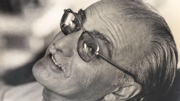 Ein Schwarz-Weiß-Foto eines grinsenden Mannes mit Brille, der mutmaßlich Mahatma Gandhi ist, mit einem unscharfen Hintergrund.