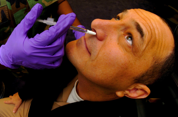 Ein Arzt in lila Handschuhen verimpft einem Mann ein Vakzin, indem er es mit einer Spritze in seinen Mund einführt.