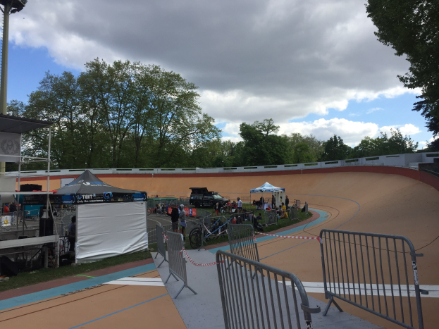 Gruppe von Radfahrern, die auf einer Schmutz-BMX-Strecke bei den UCI-BMX-Weltmeisterschaften 2018 fahren, mit Zelten, Fahrzeugen und Bäumen im Hintergrund.
