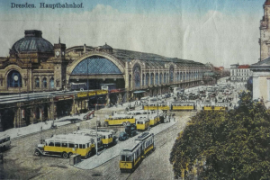 Eine sepiafarbene Postkarte des Dresdner Hauptbahnhof Bahnhofs in Deutschland, die eine belebte StraßenSzene mit Fahrzeugen, Fußgängern, Bäumen, Gebäuden und einem bewölkten Himmel zeigt.