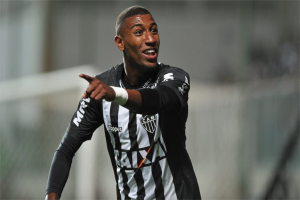 Ein Fußballspieler in einem schwarzen und weißen gestreiften Trikot lächelt, während er ein Tor feiert, mit einem unscharfen Hintergrund.