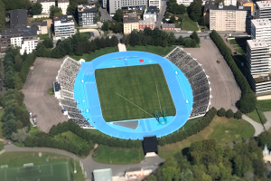 Aerial view of the Olympic Stadium in Munich, Germany, surrounded by buildings, trees, roads, vehicles, and grass.