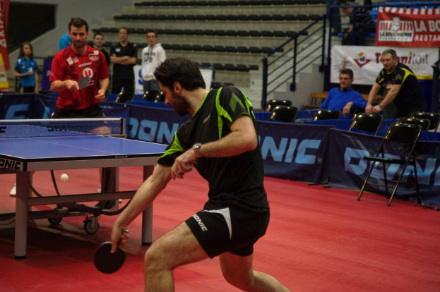 Eine Gruppe von Menschen in verschiedenen Farben, darunter Schwarz, Weiß und Blau, versammelt sich um einen Tisch mit einem im Gange befindlichen Spiel, mit Stühlen und einer Treppe im Hintergrund.