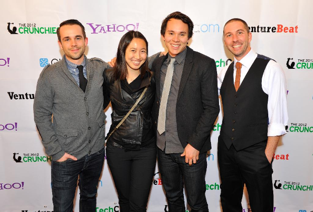 Eine Gruppe strahlender Menschen, die vor einer Sponsorentafel posieren.
