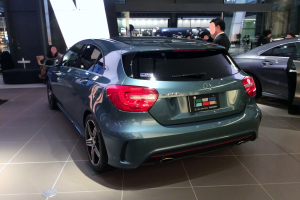 Ein Mercedes-Benz A-Klasse Hatchback auf der IAA in Frankfurt, ein schlanker, moderner Design mit glänzender schwarzer Lackierung, Chromakzenten, sportlichem Look, niedriger Profil, breiter Stand, markanter Kühlergrill und Aluminiumrädern, umgeben von einer Gruppe von Menschen.