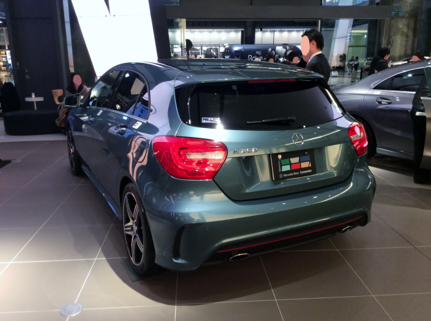 Ein Mercedes-Benz A-Klasse Hatchback auf der IAA in Frankfurt, ein schlanker, moderner Design mit glänzender schwarzer Lackierung, Chromakzenten, sportlichem Look, niedriger Profil, breiter Stand, markanter Kühlergrill und Aluminiumrädern, umgeben von einer Gruppe von Menschen.