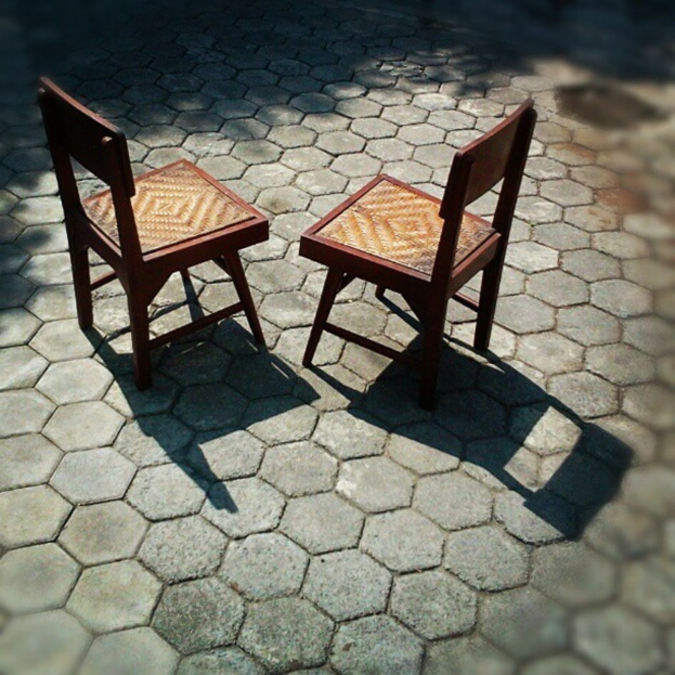 Zwei braune Stühle auf einem hellgrauen Weg.