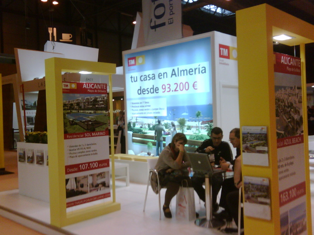 Eine Gruppe von Menschen, die um einen Tisch sitzen und auf einen Laptop schauen, mit mehreren Flyern, die verschiedene Werbeanzeigen zeigen.