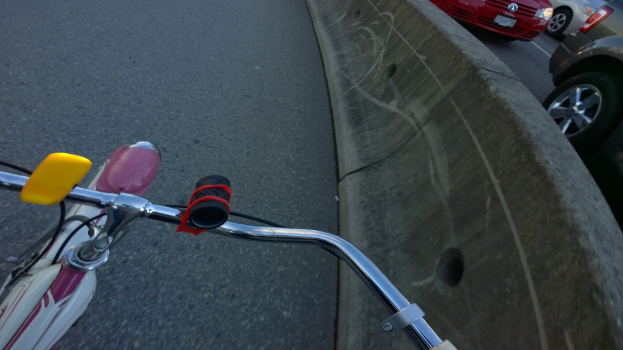 Ein Fahrradlenker unten, Fahrzeuge, die auf der Straße rechts fahren, und ein Teiler in der Mitte.
