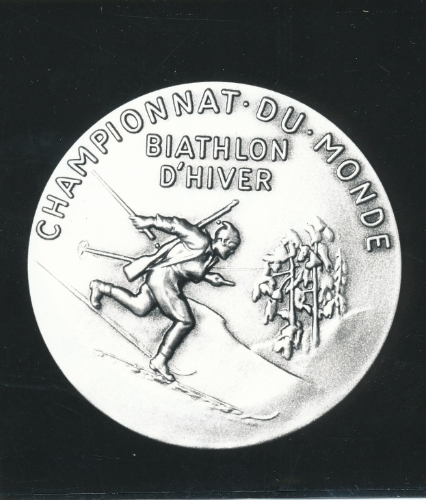 Eine Silbermedaille mit einer Abbildung eines Mannes, der Ski fährt, und einer Inschrift, vor einem schwarzen Hintergrund.