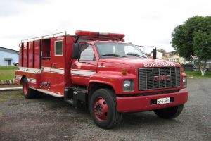 Motorisierte Fahrzeuge auf einer Straße mit Bäumen, Gras, Gebäuden und einem bewölkten Himmel im Hintergrund.